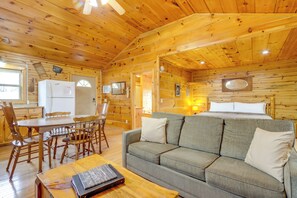 Interior de una cabaña de madera con sofá, mesa de comedor, sillas y un refrigerador.