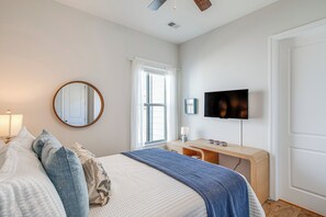 Un dormitorio con cama, escritorio, televisor y ventana con cortinas.