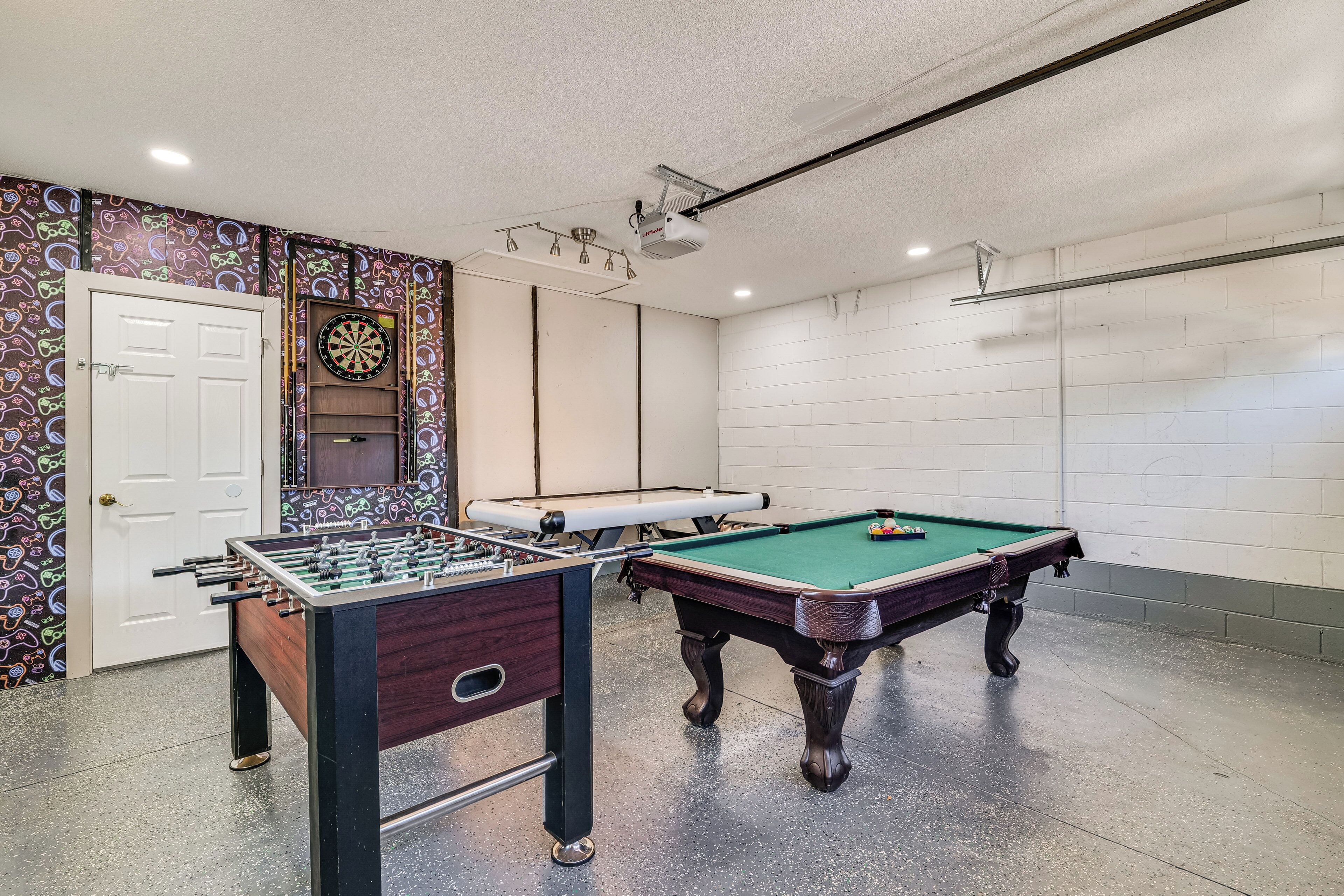 A room with a foosball table, a pool table, and a dartboard.