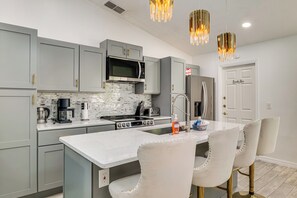 Une cuisine moderne avec des meubles gris, un îlot central, des appareils en acier inoxydable et un plan de travail blanc.