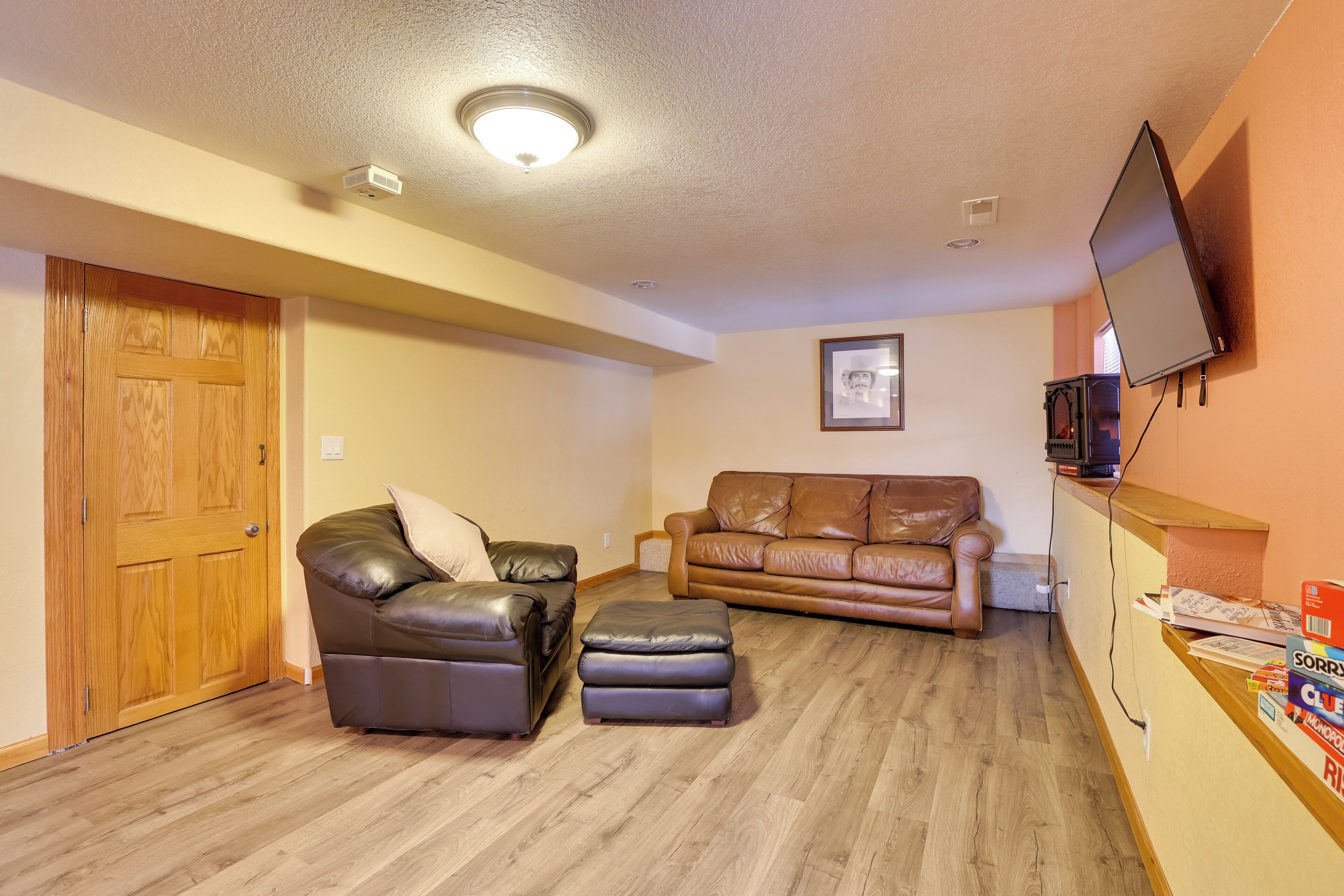 A living room with two leather sofas, a wooden door, a television mounted on the wall, and a wooden floor.