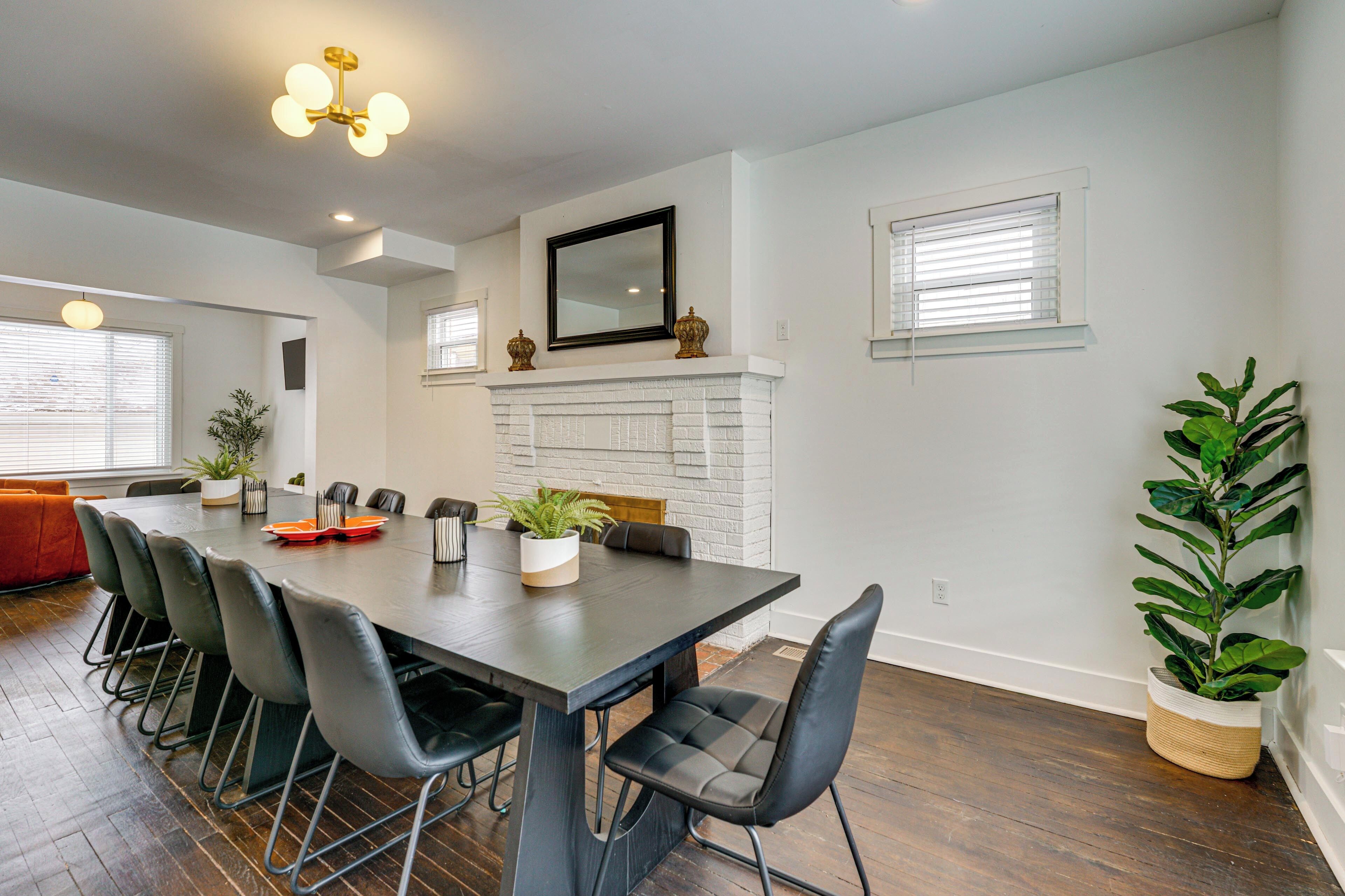 A dining area with a long table, black chairs, a white fireplace, and a large potted plant.