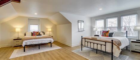 A spacious attic bedroom with two beds, wooden flooring, and large windows.