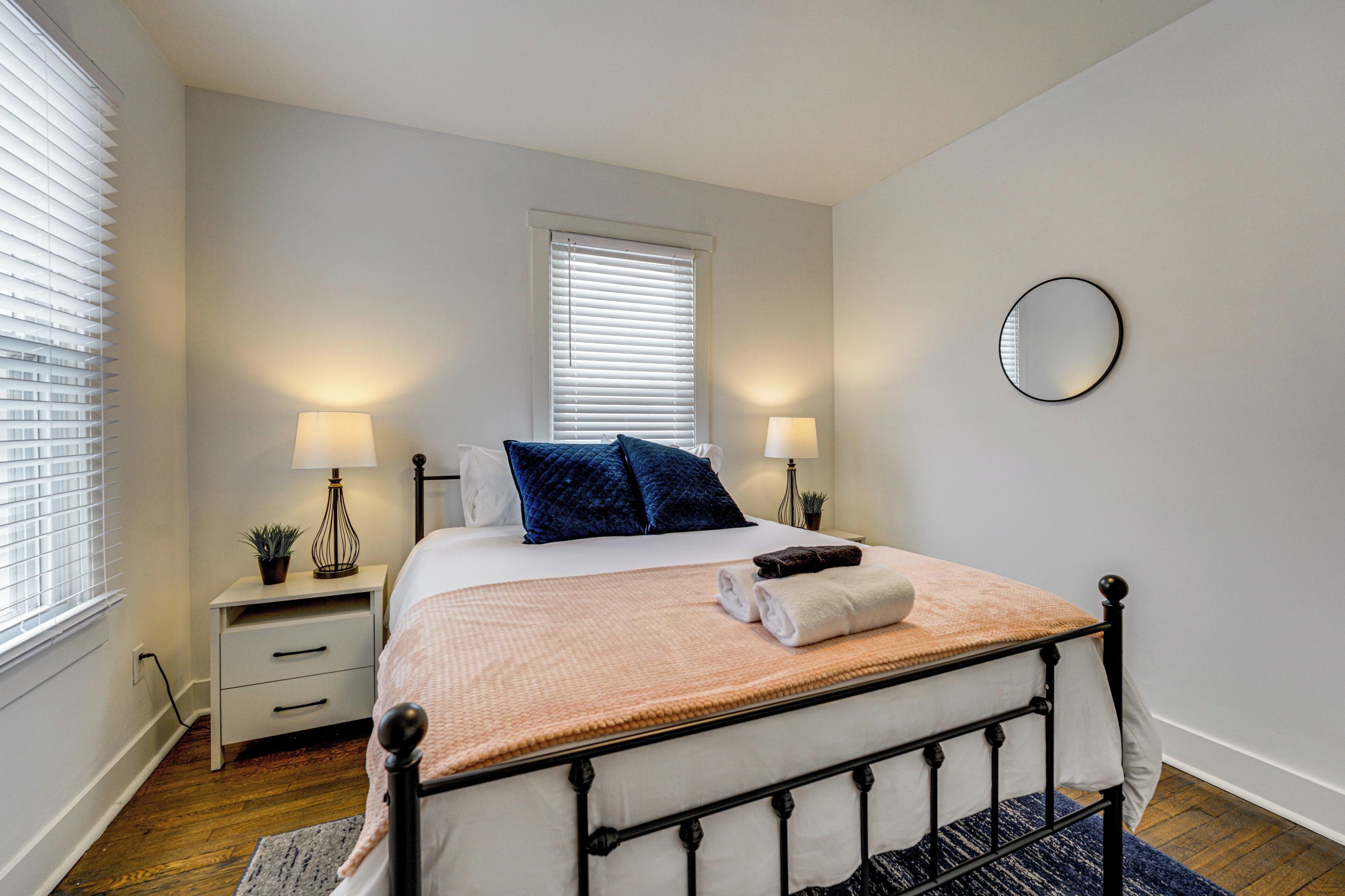 Une chambre à coucher bien rangée, avec un lit, des lampes de chevet, une petite table et une fenêtre équipée de stores.