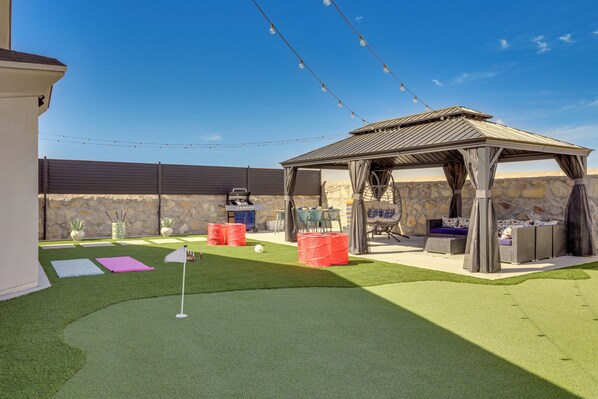 A backyard with artificial grass, a gazebo, outdoor seating, and string lights.