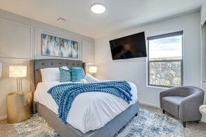 Een slaapkamer met een bed, een aan de muur bevestigde televisie, een raam en een stoel.