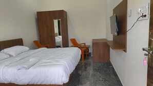 A hotel room with a bed, a wooden wardrobe, a desk with a chair, and a TV mounted on the wall. - Annamalaiyar Mahal & Residency (Chengam)