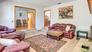 Ein Wohnzimmer mit einem braunen Ledersofa, einem passenden Hocker und einem gemusterten Teppich. An der Wand hängt ein Blumenbild und auf einem kleinen Tisch steht eine Lampe.