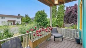 A covered porch with a wooden bench, a planter with red flowers, and a view of a residential street. - Gateway to Adventure! Dtwn Toledo Home Near Hiking (Toledo)