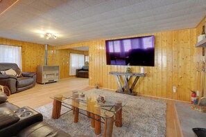 Un salon spacieux doté d’un grand téléviseur à écran plat, de murs en bois, d’un canapé en cuir et d’une table basse en verre.