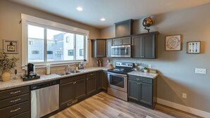 A modern kitchen with stainless steel appliances, dark cabinetry, and a large window providing natural light. - Modern Coopers Cottage w/ River Views (Billings)