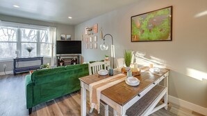 A living room with a green sofa, a wooden dining table, a TV, and a painting on the wall. - Modern Coopers Cottage w/ River Views (Billings)