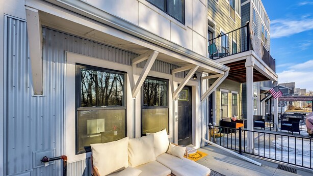 A modern building with large windows, a balcony with outdoor seating, and a visible American flag. - Modern Coopers Cottage w/ River Views (Billings)