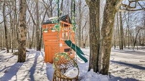 Una cabaña de madera con techo verde y una mecedora en un bosque nevado.