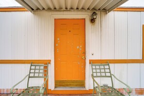 A building with a bright orange door, two green metal chairs in front, and a white and orange exterior. - Walk to Loop Trail! East Wenatchee Basecamp (East Wenatchee)