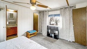 Un dormitorio con cama, ventilador de techo, ventana con cortinas, banco de madera y un mueble de almacenamiento.