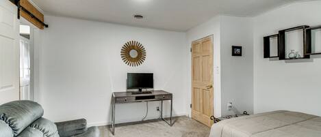 Una habitación con escritorio, silla, cama, puerta y espejo fijado a la pared.