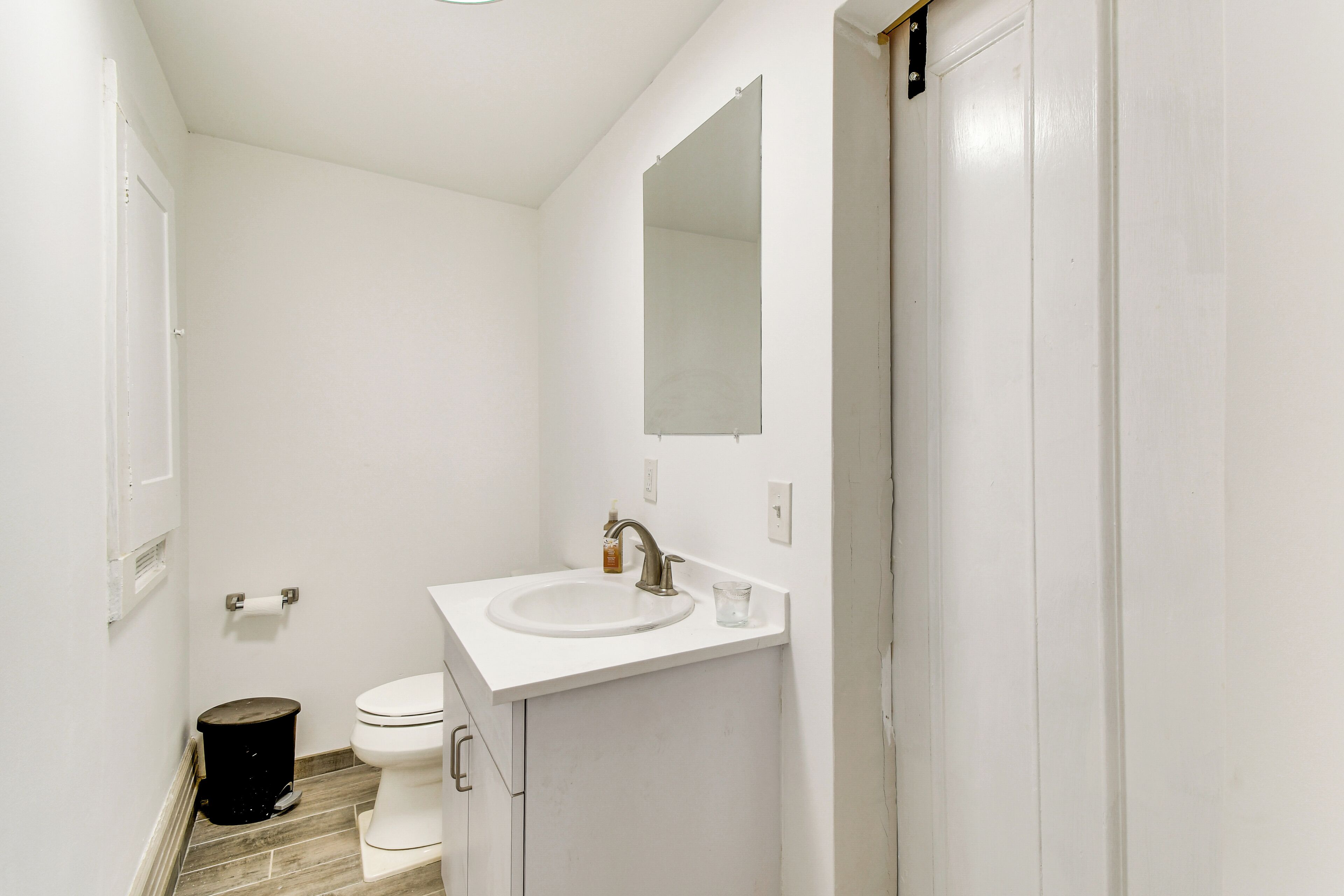 A bathroom with a white sink, a mirror, a toilet, and a trash can.