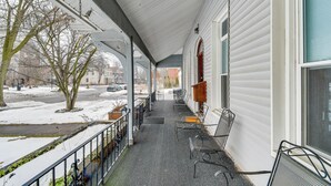 A covered porch with a view of a snowy street, metal chairs, and a building with white siding. - Explore Rochester! Charming Home 1 Mi to Downtown (Rochester)
