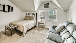 A bedroom with a bed, a bedside table, a chair, a window, and a ceiling with a skylight. - Explore Rochester! Charming Home 1 Mi to Downtown (Rochester)