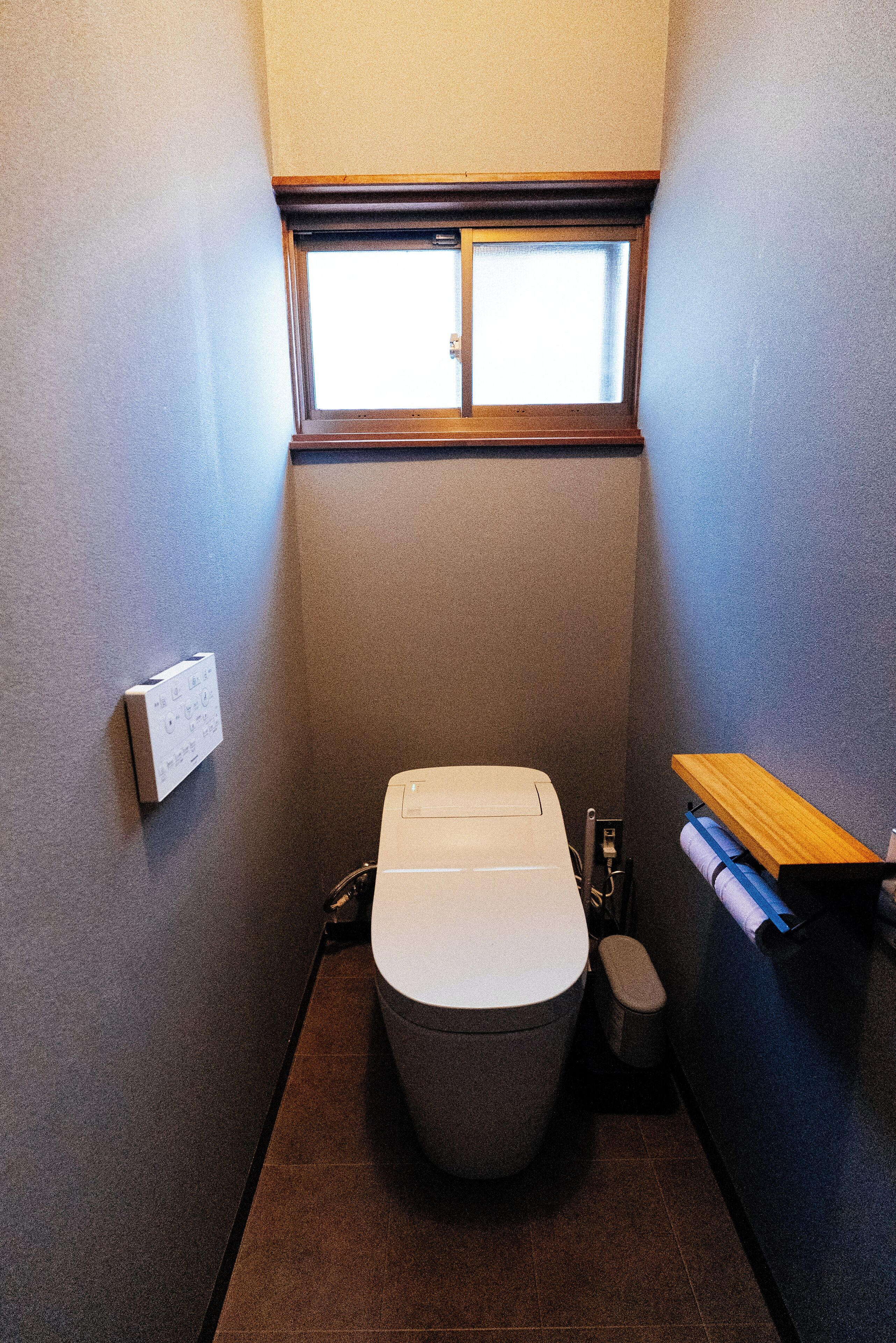 Un baño pequeño y funcional con inodoro, ventana y un estante con una toalla.