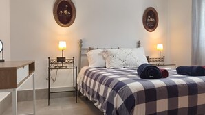 Ein ordentlich eingerichtetes Schlafzimmer mit einem Bett, zwei Nachttischen, einem Schreibtisch und zwei Wandlampen.
