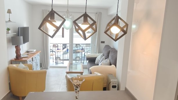 Ein modernes Wohnzimmer mit einer Couch, einem Couchtisch und einem Fernseher. Drei Pendelleuchten hängen von der Decke.