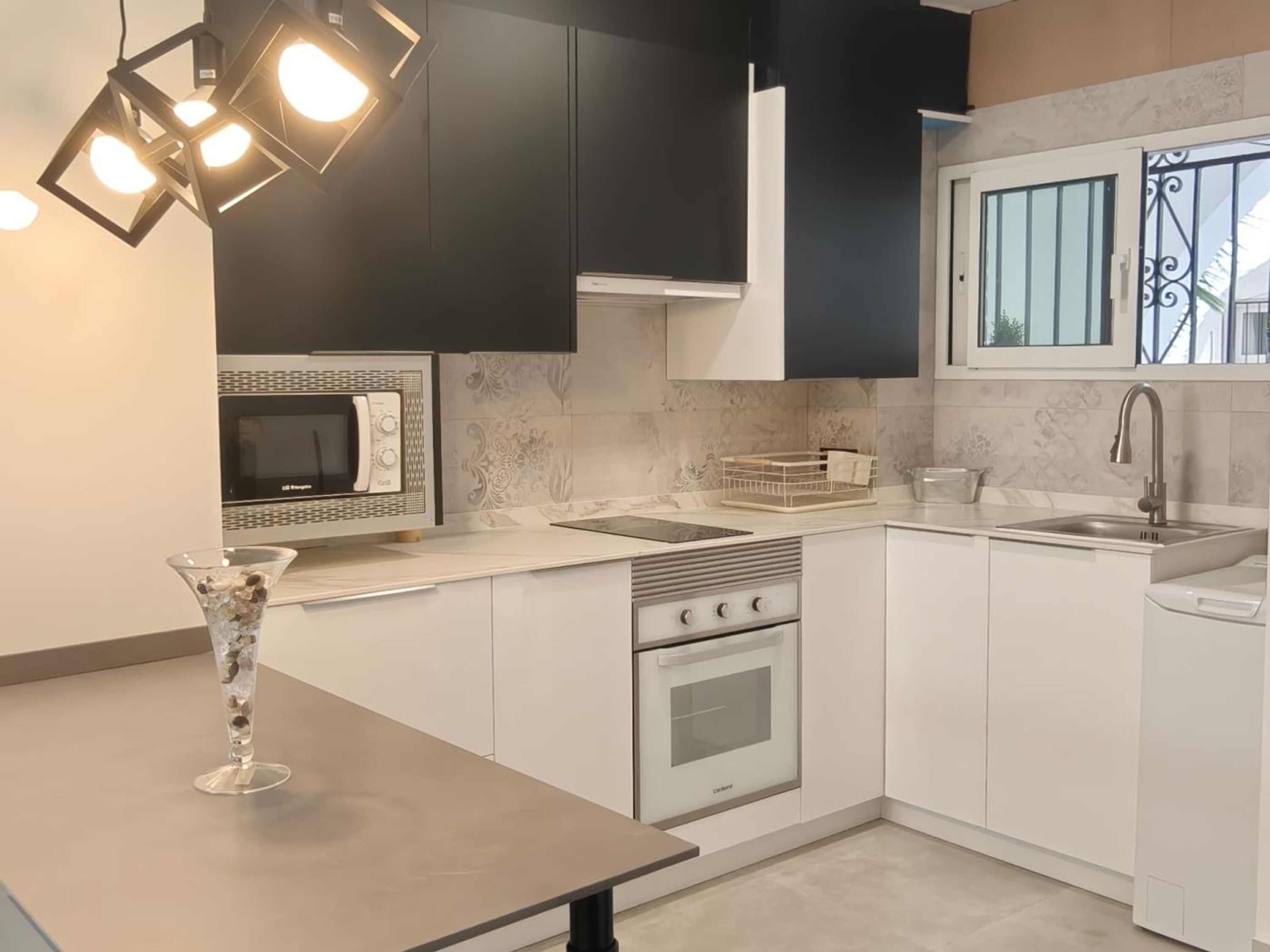 A modern kitchen with white cabinetry, a built-in microwave, a gas stove, and a window with decorative iron bars.