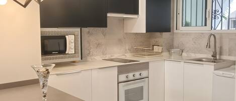 A modern kitchen with white cabinetry, a built-in microwave, a gas stove, and a window with decorative iron bars.
