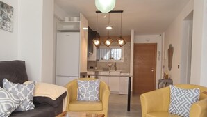 Ein modernes Wohnzimmer mit einem Glastisch, zwei Sofas und einer Küche im Hintergrund.