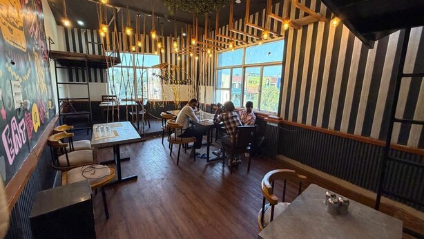 A restaurant with wooden tables and chairs, hanging light fixtures, and large windows. - The City View- Hotel And Restaurant (Bhiwani)