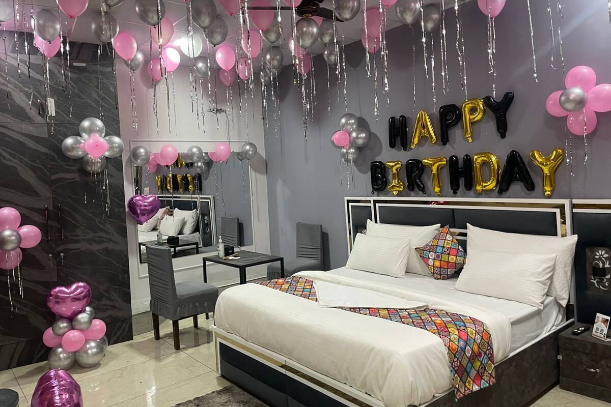 A bedroom with a bed, bedside tables, and a nightstand. There are balloons and a 'Happy Birthday' sign on the wall.