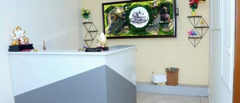 A reception desk with a check-out sign, a framed cityscape poster, and decorative items including a Buddha statue and plants.