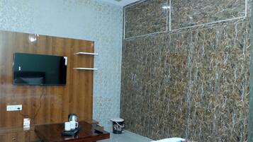 A hotel room with a wooden wardrobe, a flat-screen TV, a marble wall, a bed with a colorful quilt, and a small table with a kettle and cups.