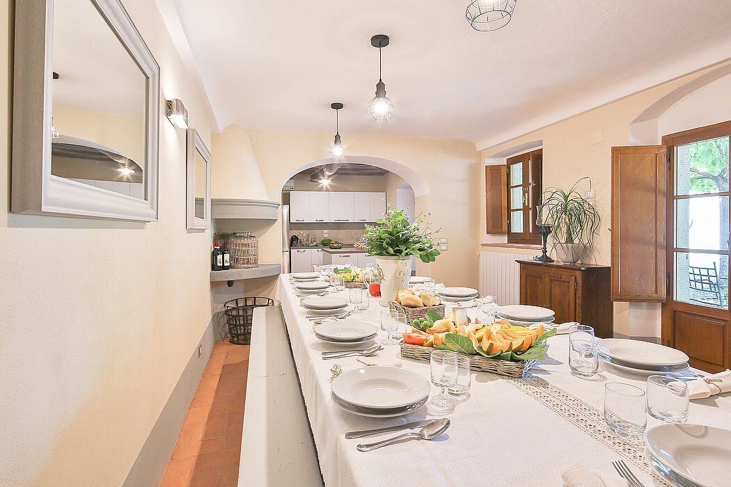 A long dining table set for a meal with plates, glasses, and a fruit basket.
