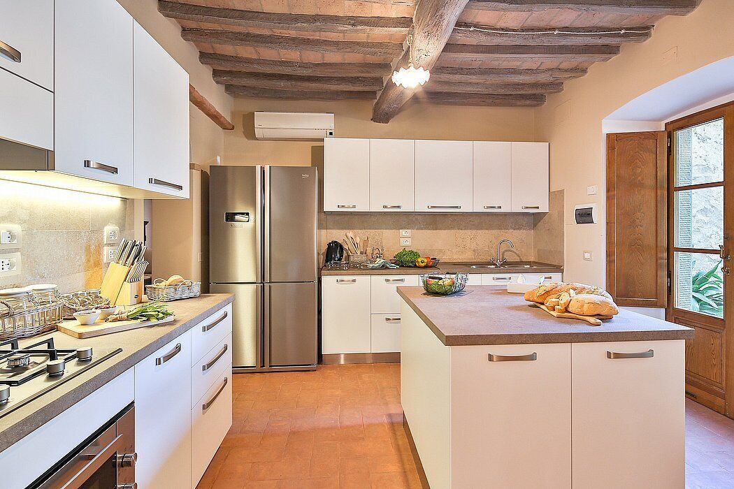 Una cucina moderna con mobili bianchi, un frigorifero in acciaio inossidabile e una grande isola con lavello.