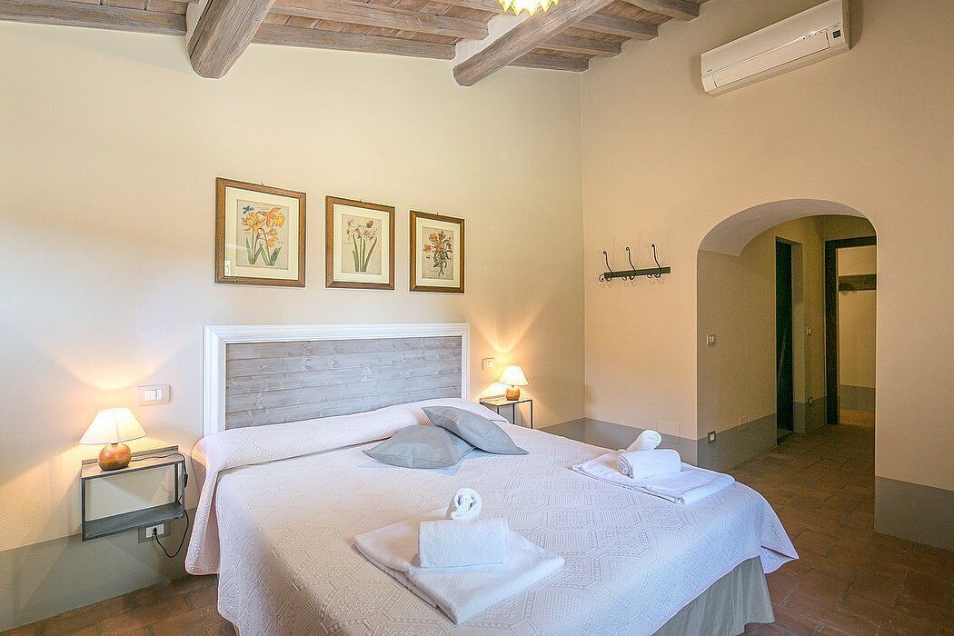 A bedroom with a large bed, two bedside lamps, and three framed floral pictures on the wall.