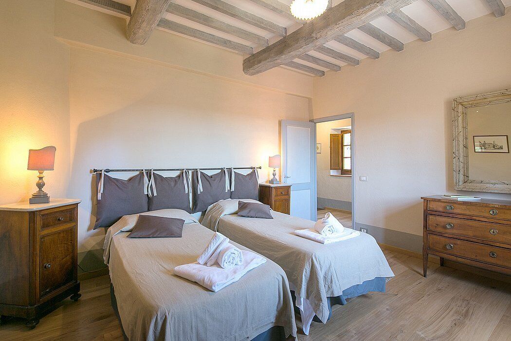 Une chambre avec deux lits, des tables de chevet en bois, une commode et un miroir au mur.