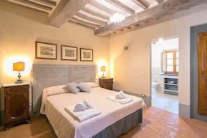 Ein Schlafzimmer mit einem großen Bett, zwei Nachttischlampen, einem Holznachttisch und einer Tür zu einem Badezimmer.