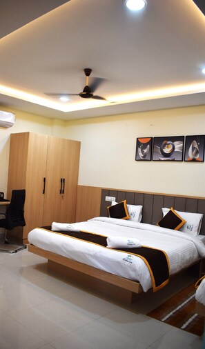A modern hotel room with a large bed, a wardrobe, a desk, and a ceiling fan. - Relax Inn Suites & Rooms (Penumuluru)