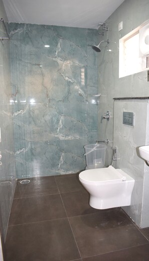 A bathroom with a marble wall, a shower, a toilet, and a sink. - Relax Inn Suites & Rooms (Penumuluru)