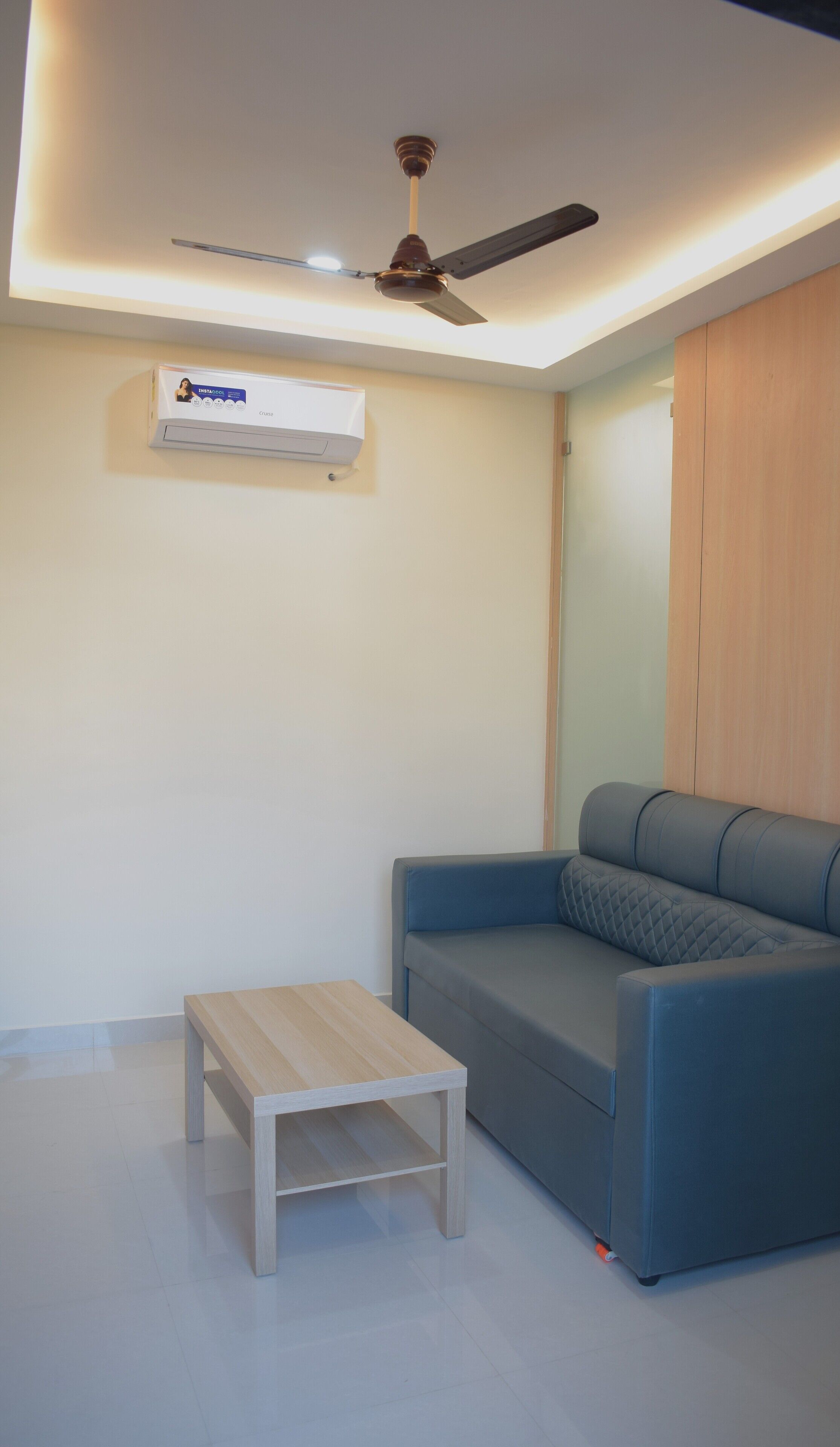 A modern living room with a blue sofa, a wooden coffee table, a ceiling fan, and an air conditioning unit.