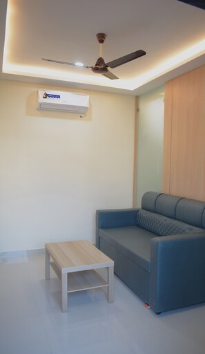 A modern living room with a blue sofa, a wooden coffee table, a ceiling fan, and an air conditioning unit. - Relax Inn Suites & Rooms (Penumuluru)