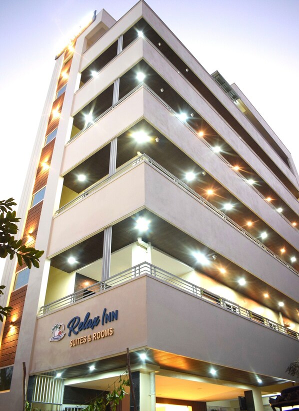 A multi-story hotel with illuminated balconies and a sign for 'Relax Inn Suites & Rooms'. - Relax Inn Suites & Rooms (Penumuluru)