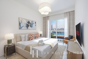A hotel room with a large bed, a TV, a view of the city, and a balcony with a pool. - LUX The Grand Bleu Suite (Dubai)