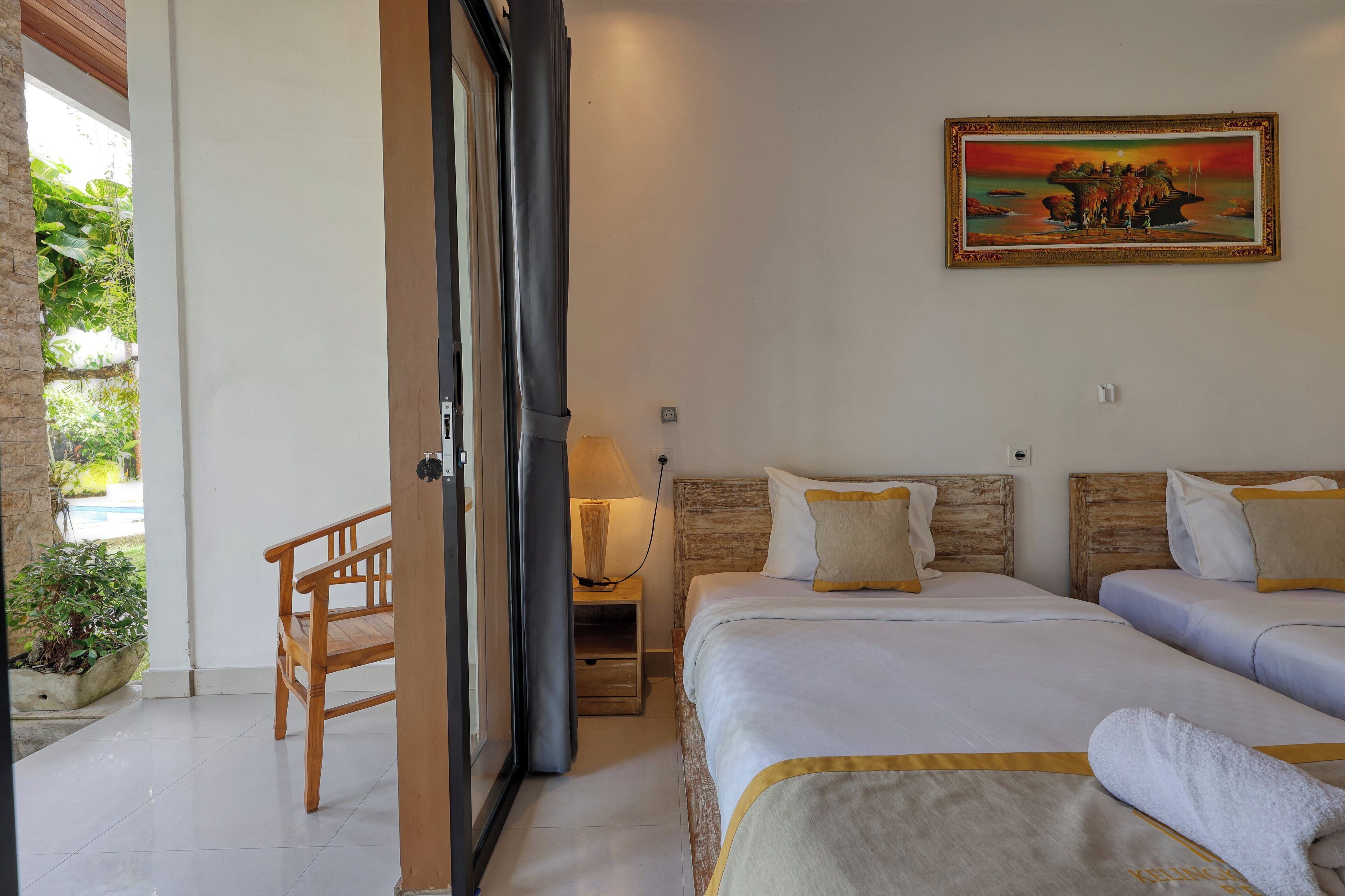 A hotel room with two beds, a wooden bench, a nightstand with a lamp, and a painting on the wall.