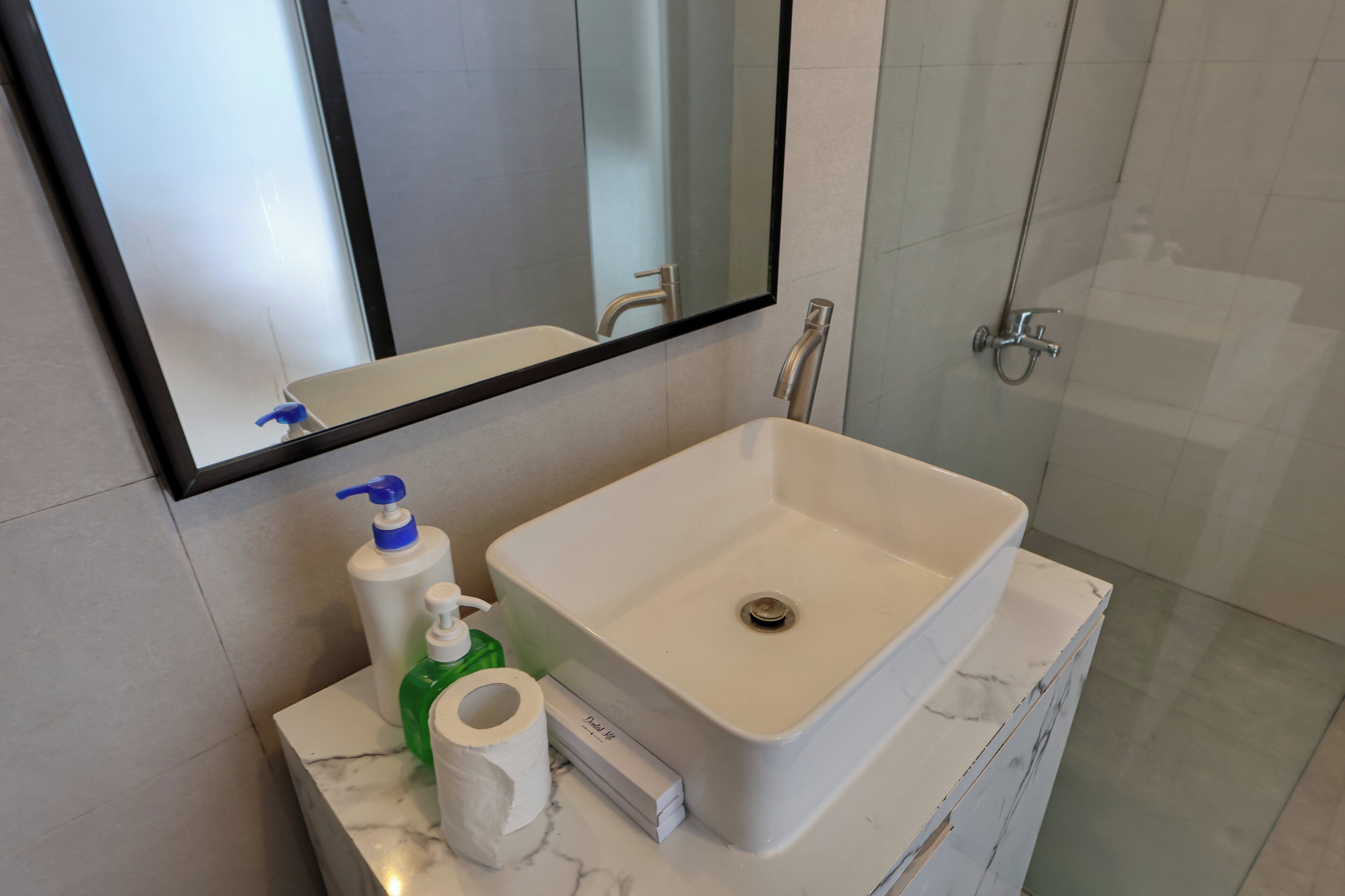A bathroom with a white sink, a mirror, a shower, and toiletries on the counter.