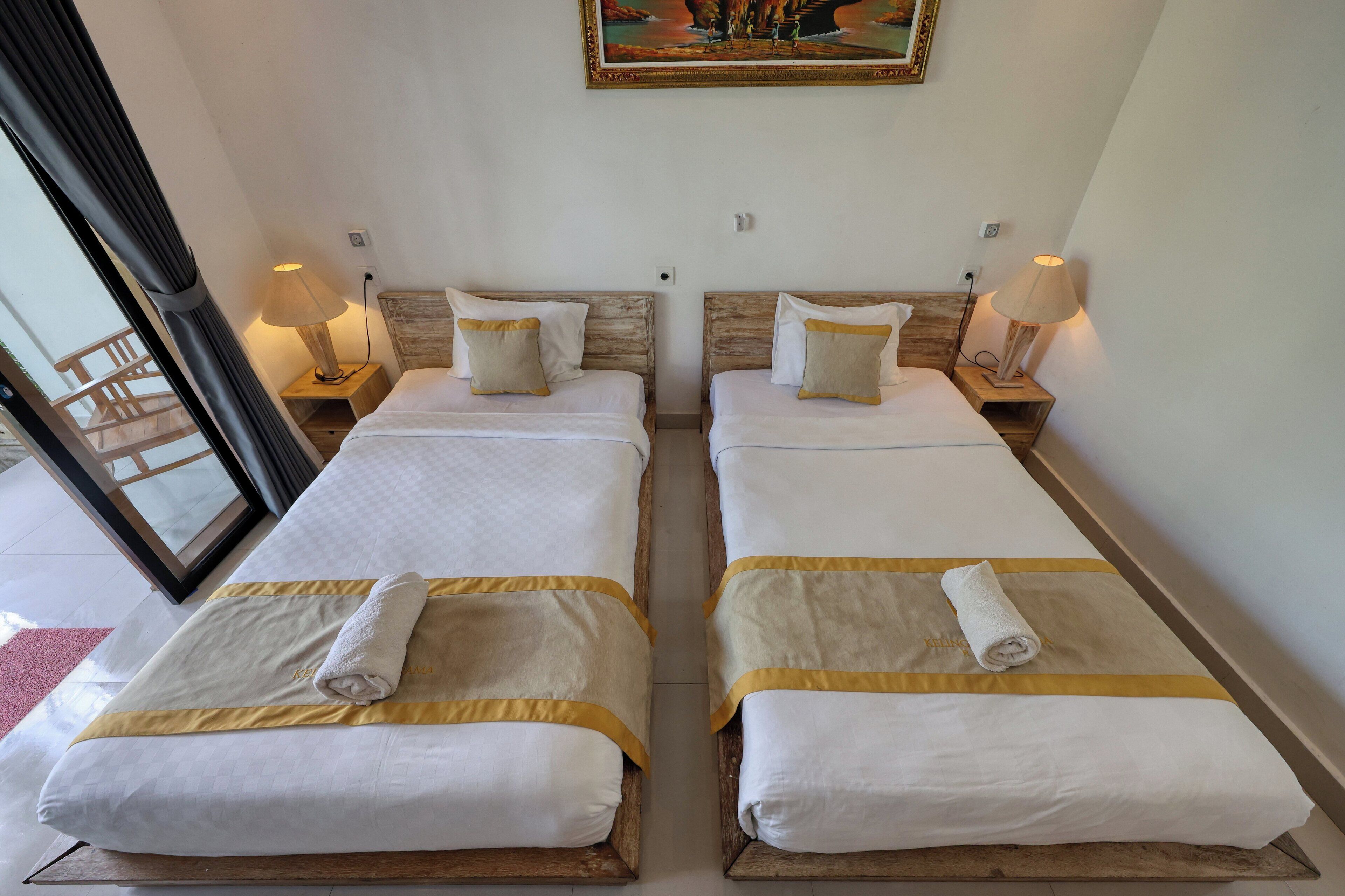 A hotel room with two beds, each with a white bedspread and a gold accent, a painting on the wall, and a window with a view.