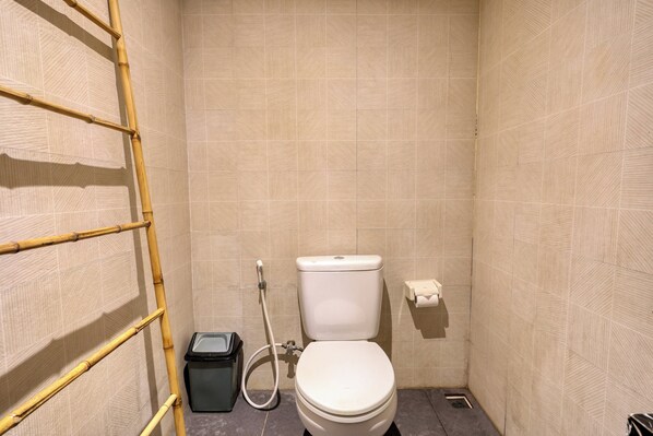 A small, tiled bathroom with a toilet, a trash bin, and a bamboo ladder. - Kelingking Point (Penida Island)