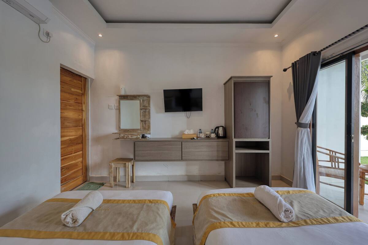 Une chambre d’hôtel avec deux lits, une télévision, une armoire en bois, une petite table et un balcon avec une chaise.
